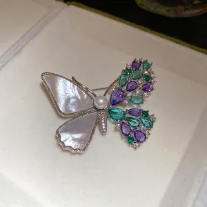Elegant asymmetric butterfly brooch featuring zircons, shell inlay, and a central pearl