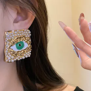Detail shot of vintage square pearl earrings with a green evil eye motif design