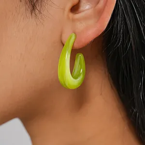 Detailed macro view of a lime green swirly resin C-shaped hoop earring worn on an ear
