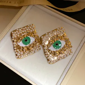 Close-up of vintage royal style rhombus earrings with pearls and green evil eye enamel detail.