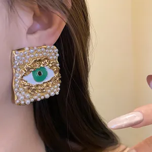 Close-up view of a vintage gold earring with pearl inlay and a green eye motif design.