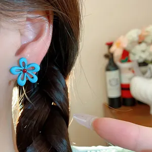 Primo piano di un orecchino a fiore blu smaltato indossato sull'orecchio di una modella