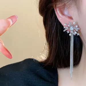 Close-up of silver-toned firework tassel earrings with pearls and crystals on ear.