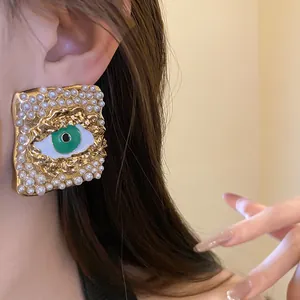 Close-up detail of vintage square gold earring with pearls and green evil eye enamel