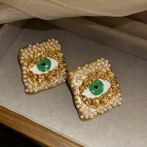 Vintage-style evil eye stud earrings with pearls and green enamel in gold finish.