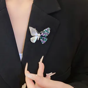 Detailed macro view of an asymmetric butterfly brooch with shell and zircons on a black blazer.