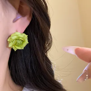 Primo piano di un delicato orecchino a perno a forma di rosa verde indossato all'orecchio
