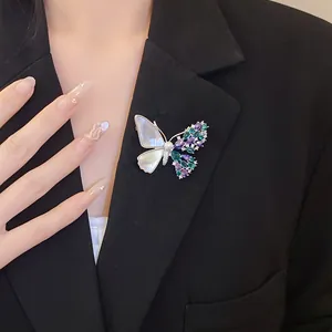 Detail of an asymmetric butterfly brooch with zircon, shell, and pearl on a black blazer.