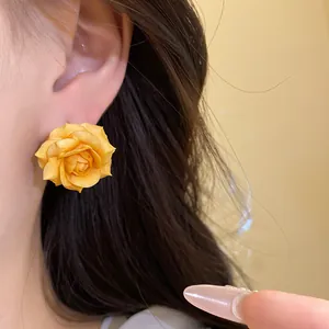 Primo piano di un orecchino a perno a forma di rosa gialla indossato sull'orecchio.