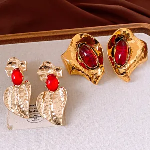 Dettaglio di orecchini vintage a foglia d'oro con pietre in resina rossa su lino