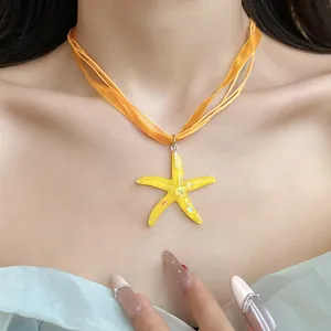 Primo piano di una collana con ciondolo a stella marina in resina e nastro arancio.