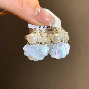 Close-up detail of iridescent shell-shaped stud earrings with delicate pearl bead accents