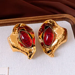 Dettaglio di orecchini vintage dorati con pietre ovali in resina rossa e design a foglia.