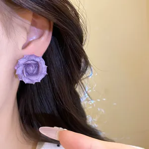 Dettaglio di un orecchino a perno a rosa viola con petali strutturati indossato sul modello.