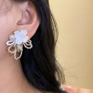 Close-up view of white gardenia flower beaded stud earring worn on model's ear with dark hair