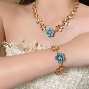 Detail of blue enamel flower necklace and bracelet set with golden finish on model.