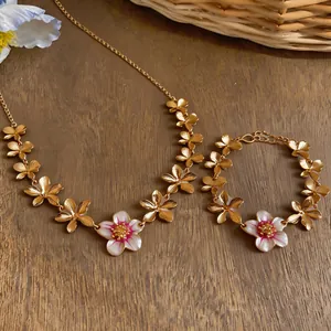 Detailed close-up of golden necklace and bracelet set with pink enamel flower charms