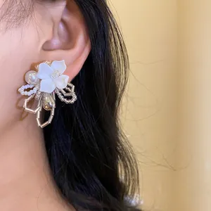Close-up of white gardenia beaded flower earrings featuring pearls and metallic details.