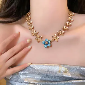 Detail shot of a gold flower necklace with a central blue enamel blossom pendant.