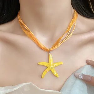 Dettaglio del ciondolo a stella marina in resina gialla con collana girocollo in nastro arancione