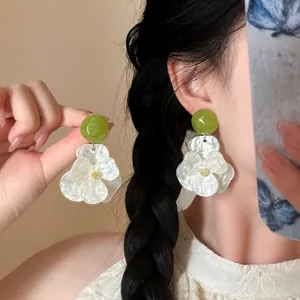 Macro detail of white iridescent gardenia flower earrings with a vibrant green bead