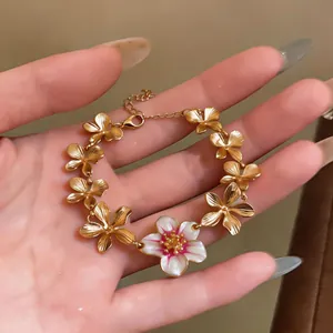 Detailed view of hand wearing a gold-plated bracelet featuring white and pink enamel flower charms
