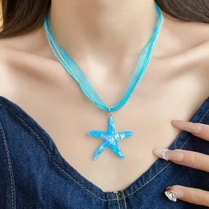Dettaglio di una collana con ciondolo a stella marina in resina blu e nastro organza
