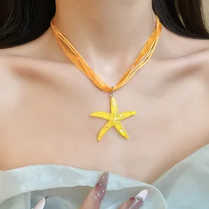 Primo piano di un ciondolo a stella marina in resina su una collana di organza arancione