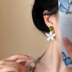Close-up view of elegant gardenia flower stud earrings featuring a green bead accent