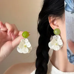 Close-up detail of white gardenia flower earrings with green studs worn by a model