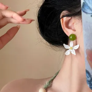 Close-up of white gardenia flower earrings with green bead in elegant New Chinese style.