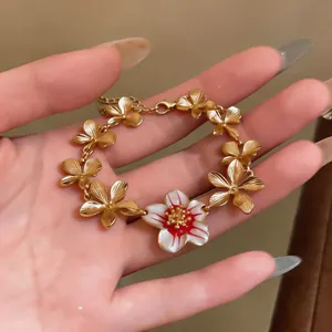 Close-up of elegant gold plated floral bracelet with a white enamel charm on a hand