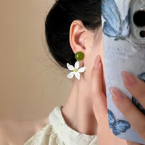 Detailed close-up of gardenia flower earrings with green bead and white petals worn on ear