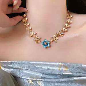 Close-up detail of a minimalist golden chain necklace with a blue enamel flower pendant