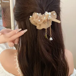Dettaglio di un elastico per capelli in organza beige con perle e ciondoli a fiore sui capelli