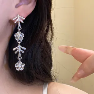 Primo piano di orecchini pendenti a forma di fiore d'argento su orecchio di modella.