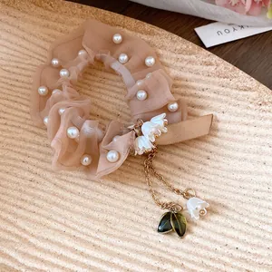 Vista dettagliata di elastico per capelli in organza beige con perle e ciondoli a mughetto.