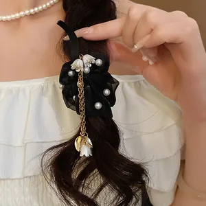 Dettaglio elastico in chiffon nero con perle e nappa a forma di mughetto.