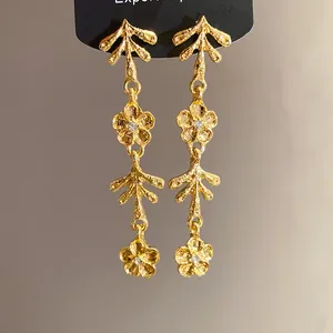 Dettaglio di orecchini pendenti a fiore dorato irregolare stile vintage con cristalli