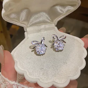 Elegantes pendientes de lazo de plata con cristales brillantes en una caja de concha.