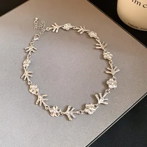 Dettaglio della collana in metallo argentato con motivi di fiori e rami irregolari.