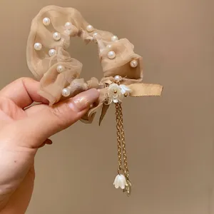 Dettaglio dell'elastico in garza beige con perle e nappa a fiori dorati