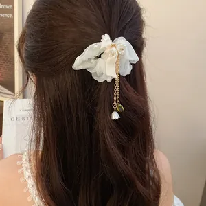 Vista dettagliata dell'elastico in chiffon bianco con perle e nappa dorata sui capelli