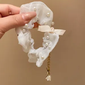 Vista dettagliata di un elastico in organza bianca con perle e nappa a fiore dorata