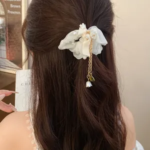 Primo piano di un elegante elastico in chiffon bianco con perle e nappa dorata sui capelli