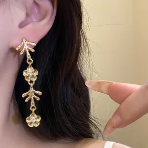Dettaglio di eleganti orecchini a sospensione dorati con fiori su una modella asiatica