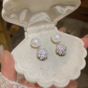 Primer plano de elegantes pendientes de perlas francesas con dijes redondos de pedrería