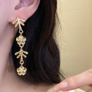 Primo piano di eleganti orecchini pendenti dorati con fiori irregolari e dettagli in cristallo.