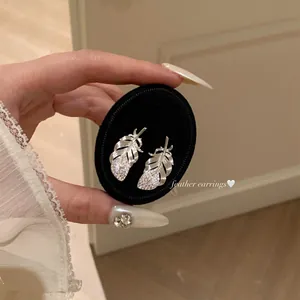 Close-up of elegant silver feather stud earrings with sparkling diamonds