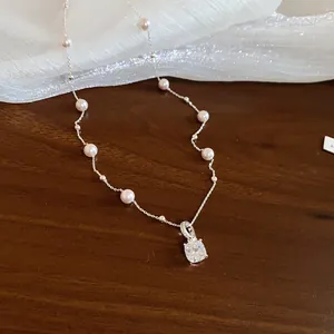 Detailansicht einer Perlenkette mit quadratischem Zirkonia-Anhänger auf Holzgrund.